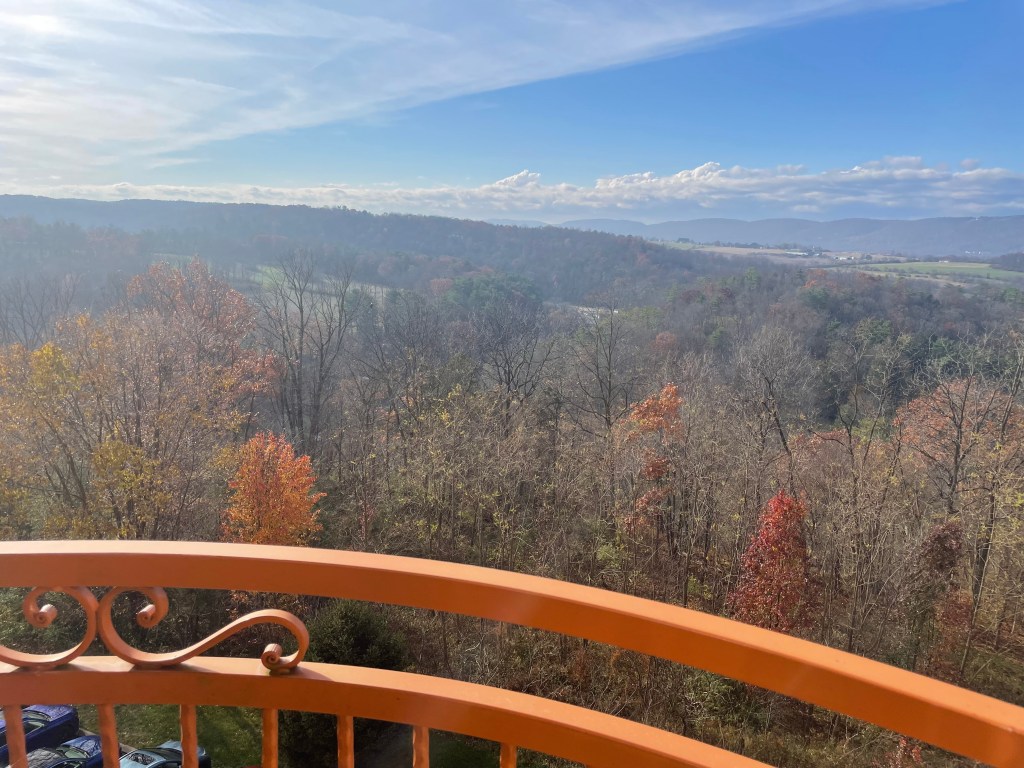 View of colorful autumn foliage and rolling hills from a balcony railing against a clear blue sky.